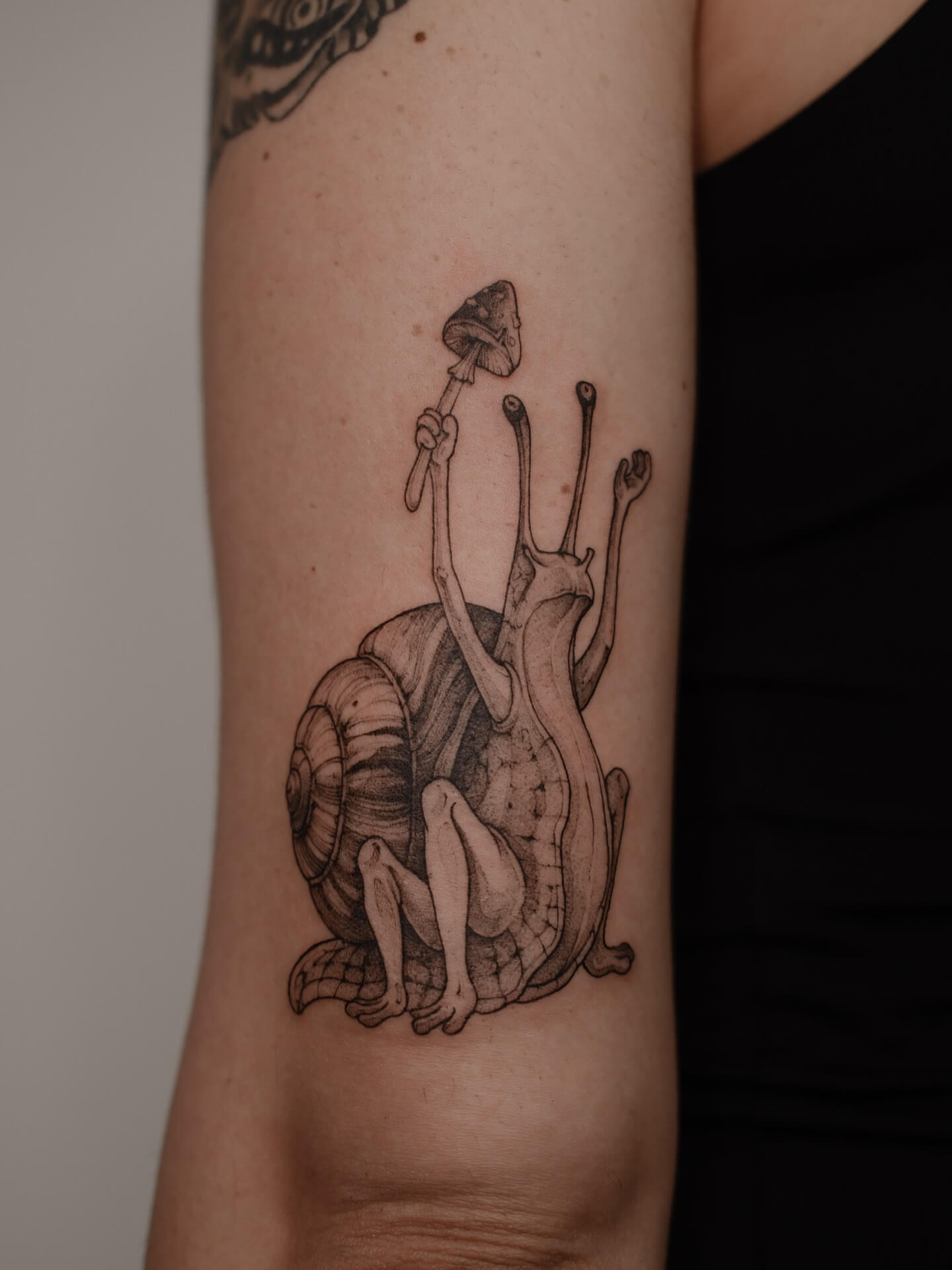 Graphic tattoo of a snail with a human figure holding a mushroom on forearm — tattoo Barcelona