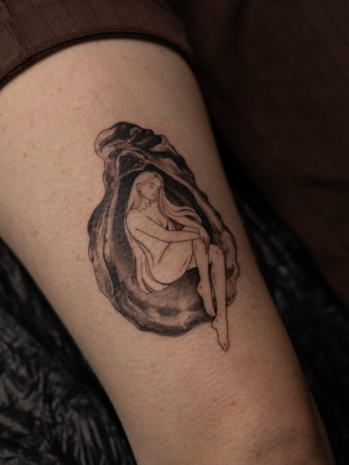 Fine line tattoo of a woman figure inside an oyster shell on inner arm — tattoo Barcelona